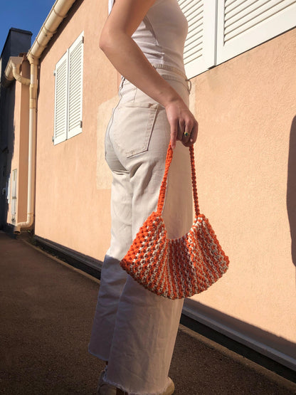 sac à main en macramé orange et blanc porté par une femme